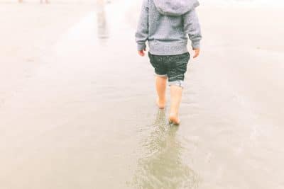 Criança andando descalça na areia.